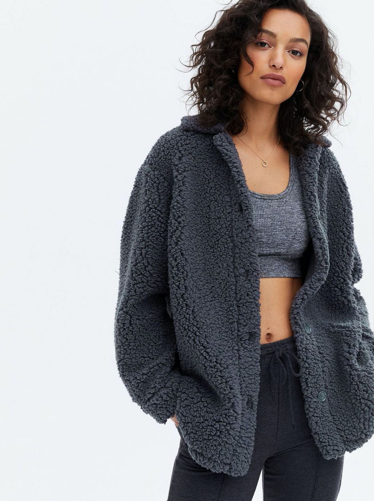Woman wearing a dark grey teddy shacket, crop top and trousers