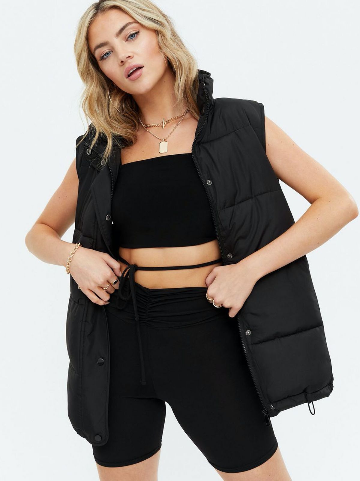 Woman wearing a black high neck padded gilet, black jacket and cycling shorts