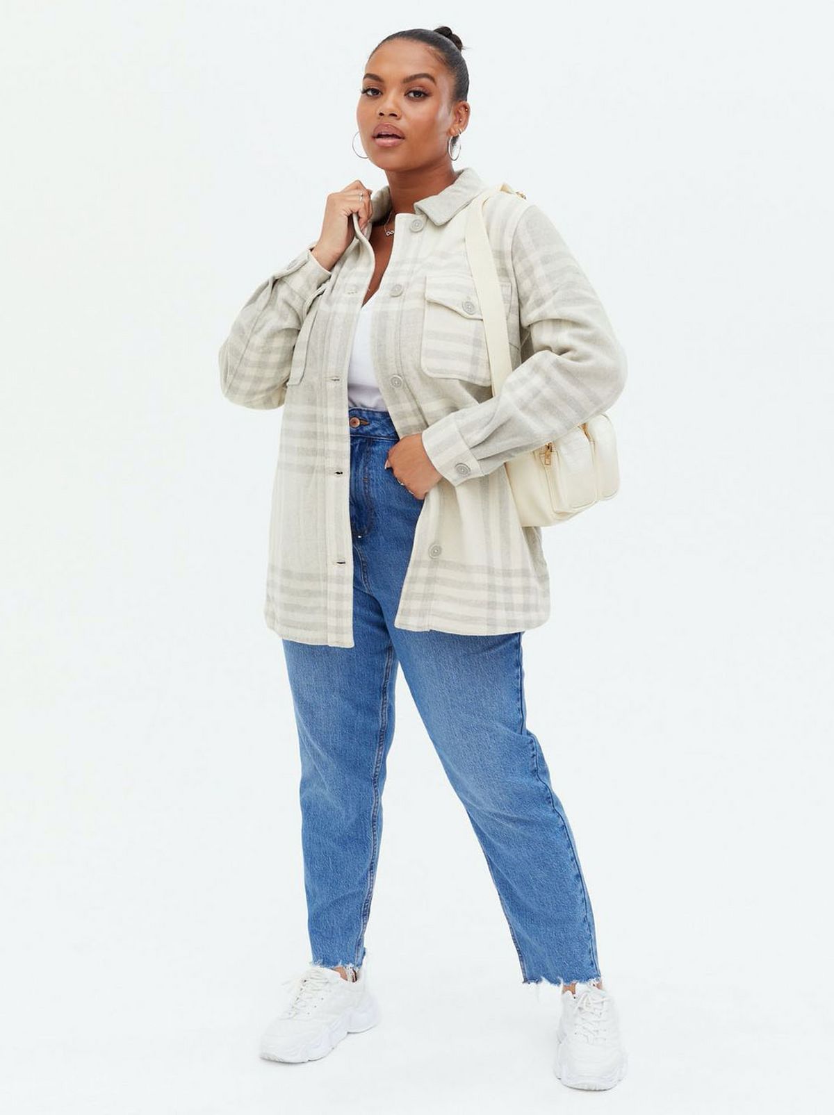 Woman wearing a light grey check shacket, white top, blue jeans and trainers