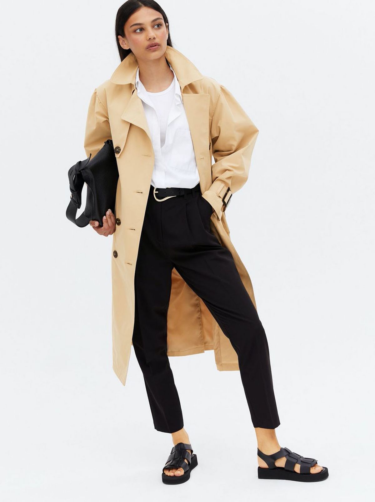 Woman wearing a stone puff sleeve belted trench coat, white blouse, black trousers and sandals