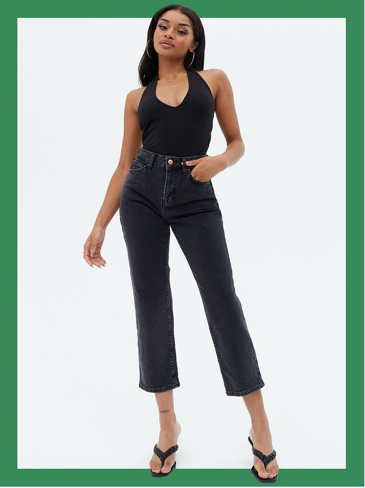 Woman wearing black dark wash ankle grazing straight leg jeans, black vest to and heels