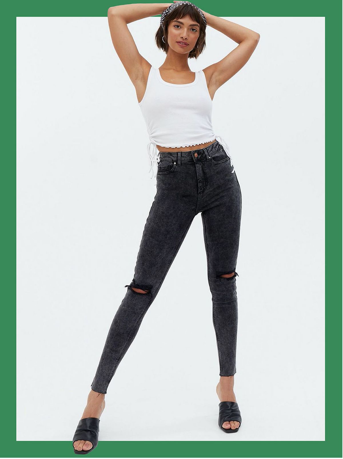 Woman wearing black acid wash high rise skinny jeans, white vest top and heels