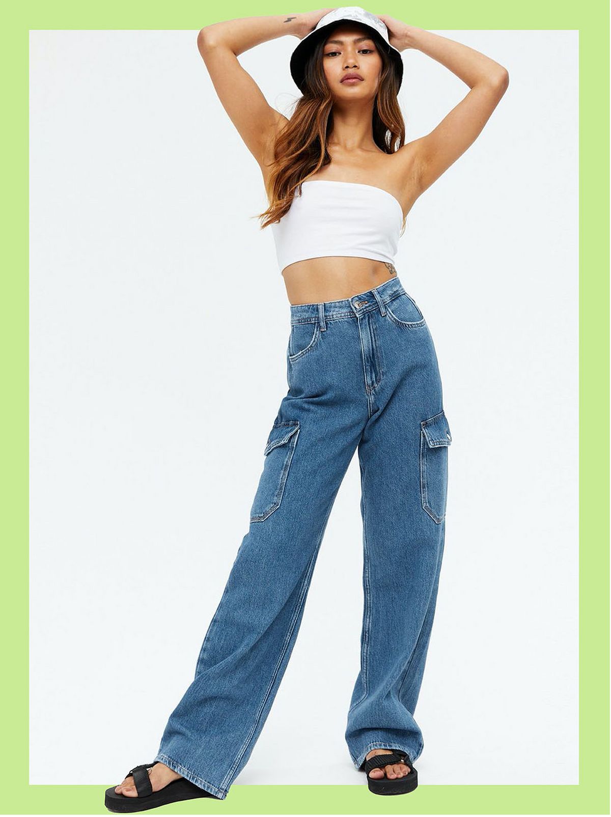 Woman wearing blue cargo pocket 90s baggy fit jeans, crop top, sandals and a bucket hat