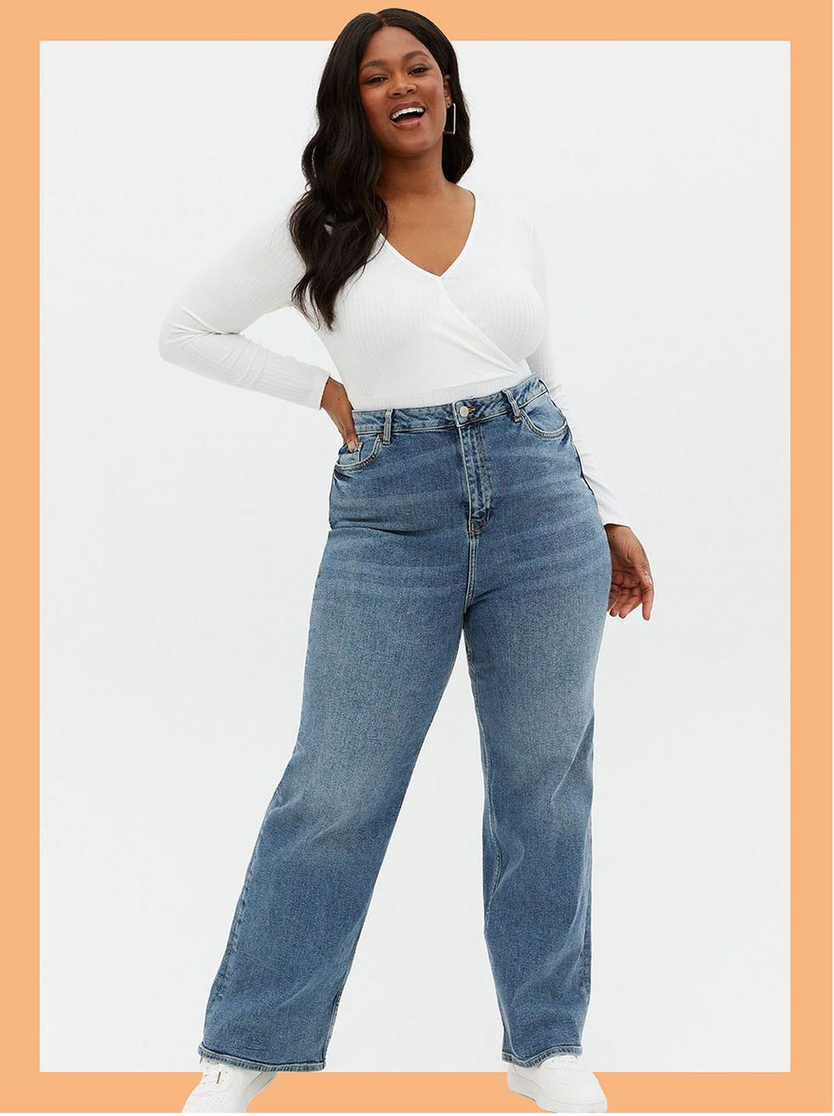 Woman wearing blue high rise baggy fit jeans, white long sleeve top and trainers