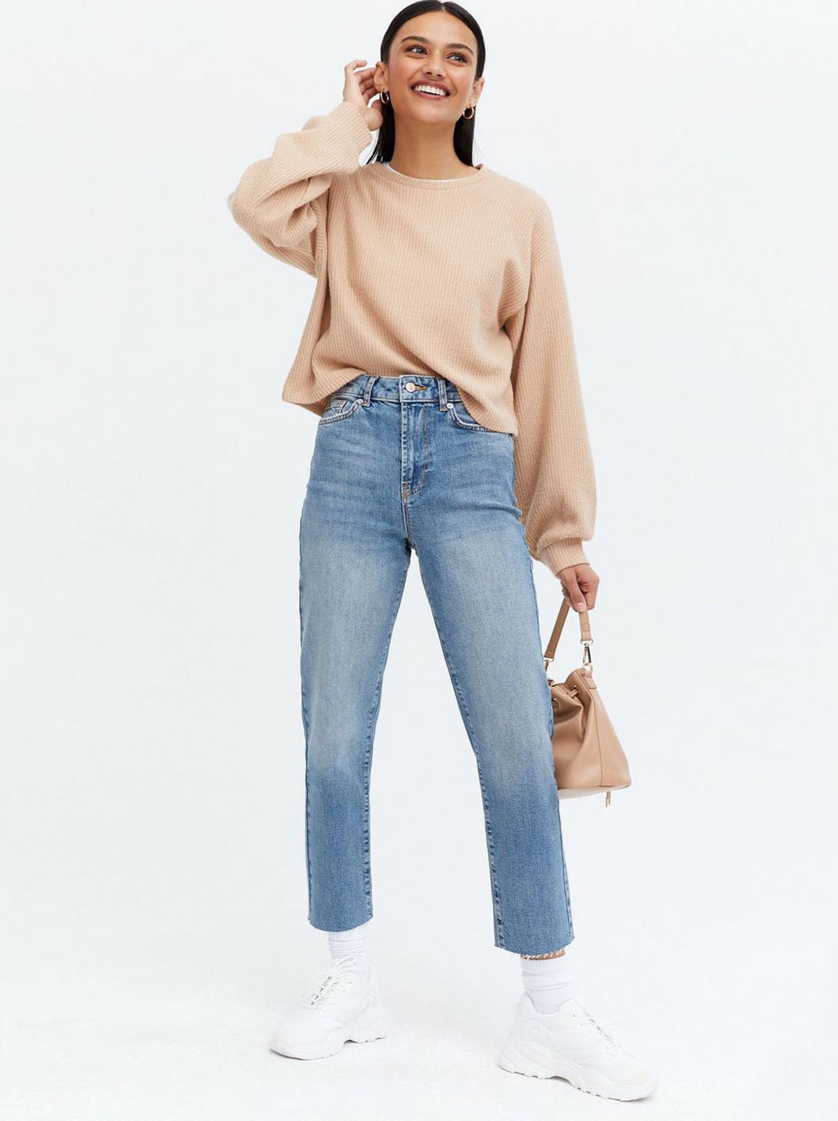 Woman wearing blue ankle grazing straight leg jeans, peach jumper and trainers