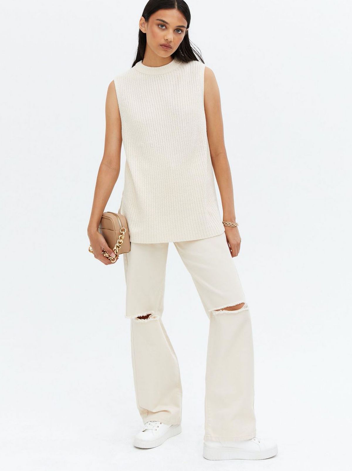 Woman wearing a off white ribbed long step hem vest jumper