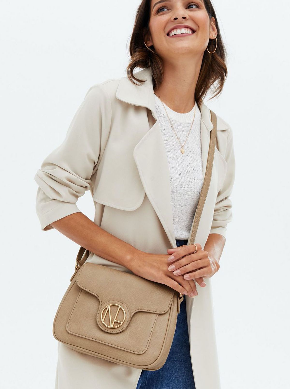 Woman carrying a cream leather look cross body bag wearing a cream coat, white top and jeans