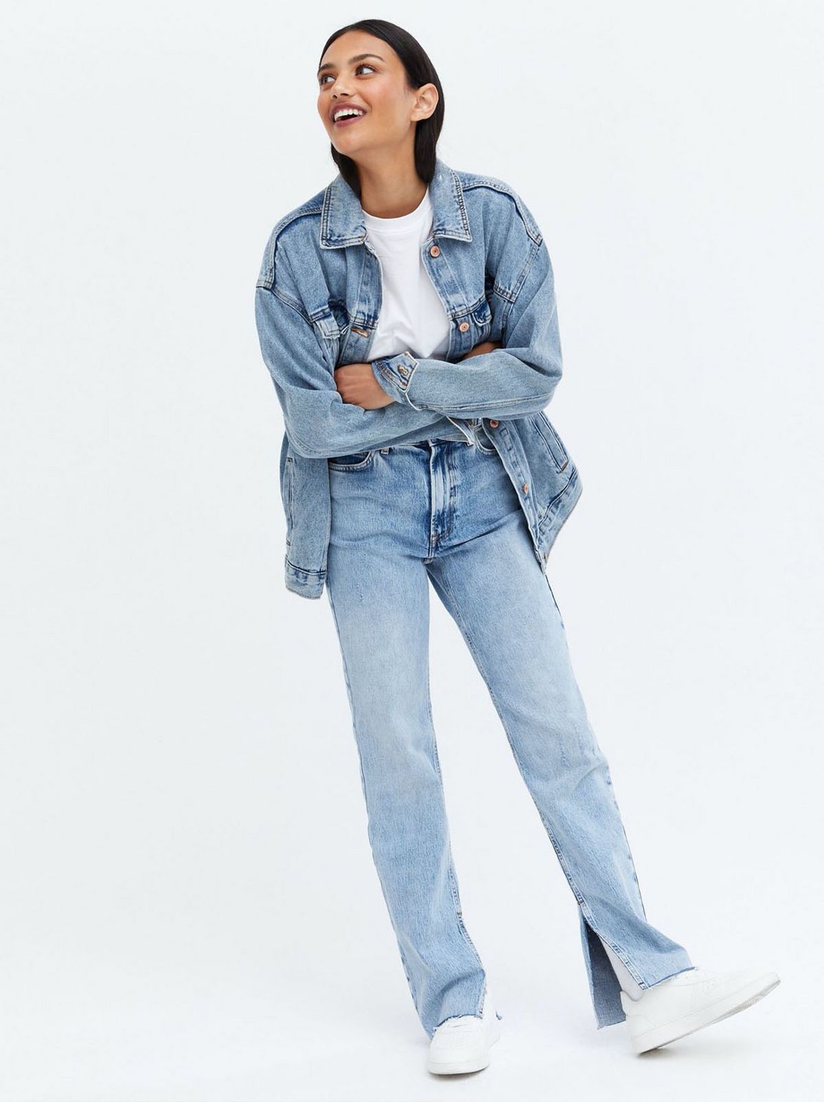 Woman wearing a blue long split straight leg jeans, denim jacket, t-shirt and trainers