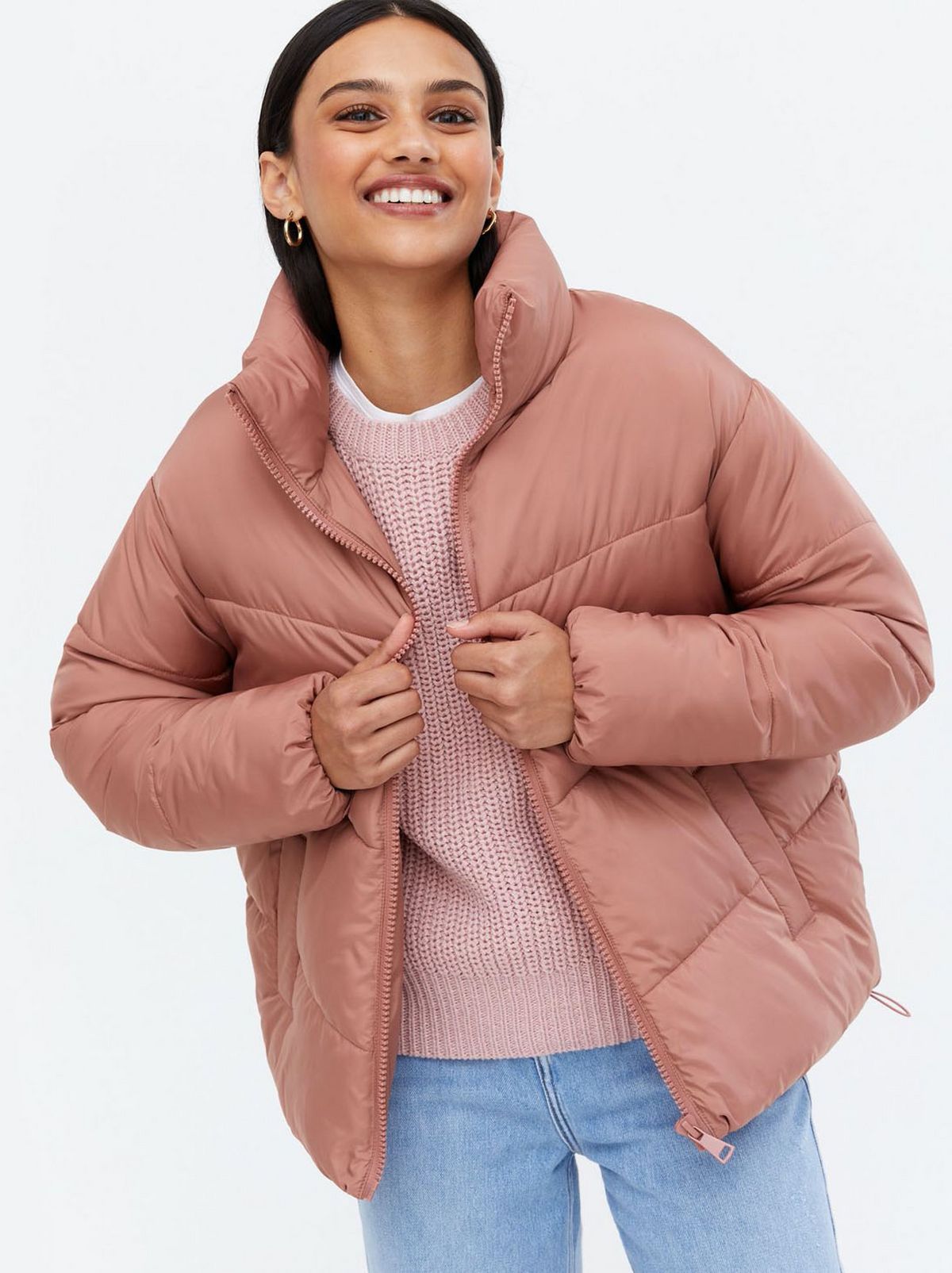 Woman wearing a deep pink boxy puffer jacket, pink jumper and jeans