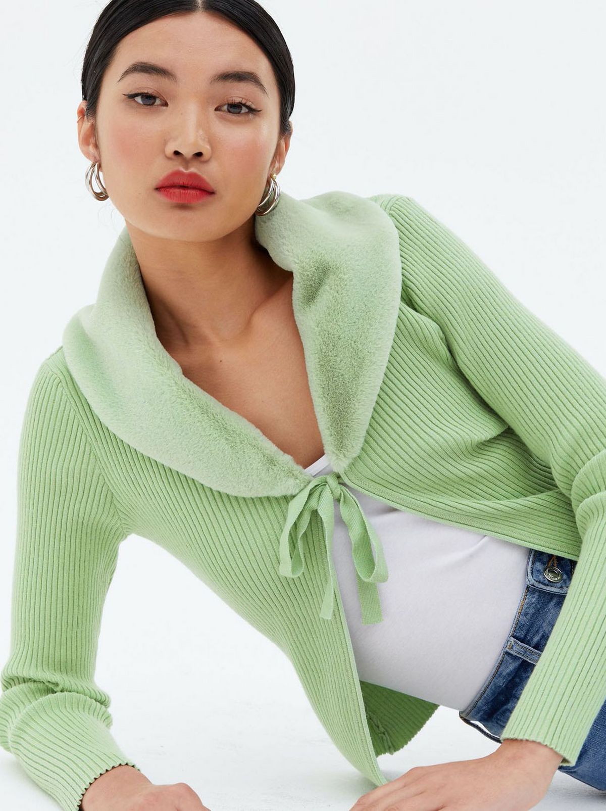 Woman wearing a green ribbed knit faux fur trim cardigan, top and jeans