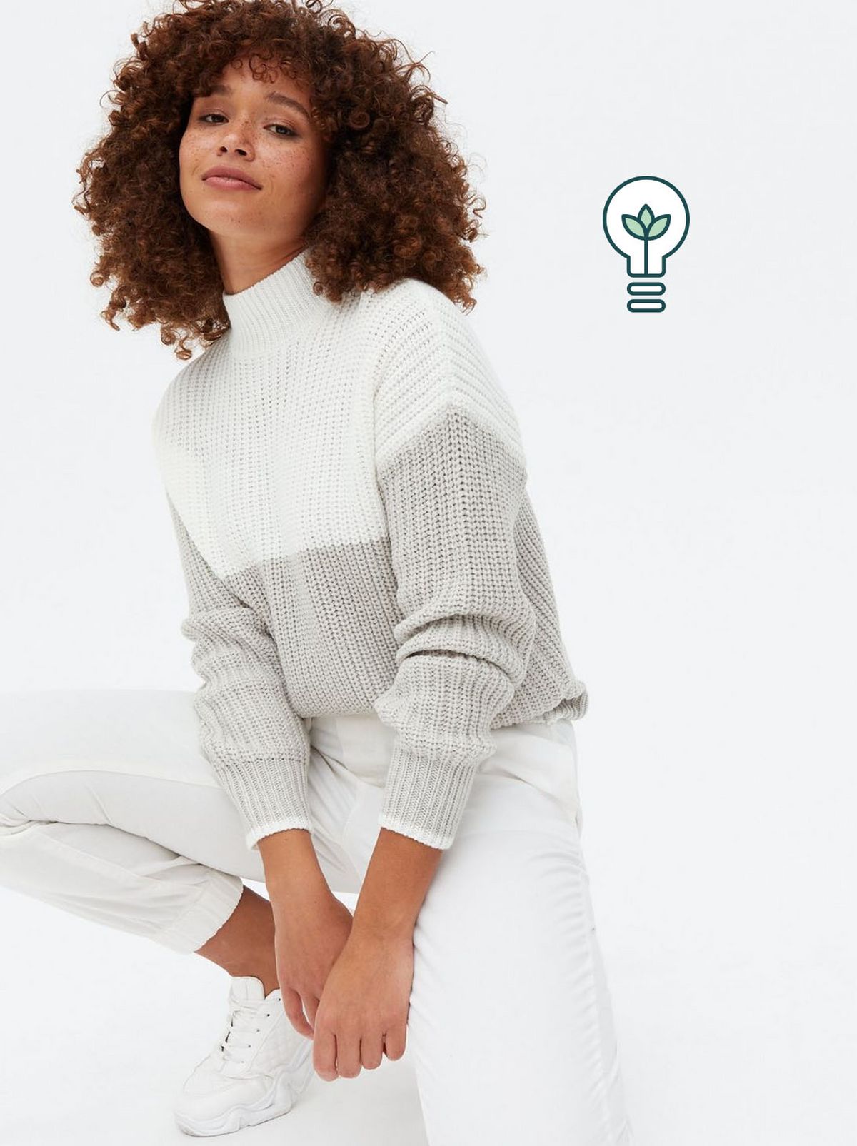Woman wearing a grey high neck jumper, white jeans and trainers