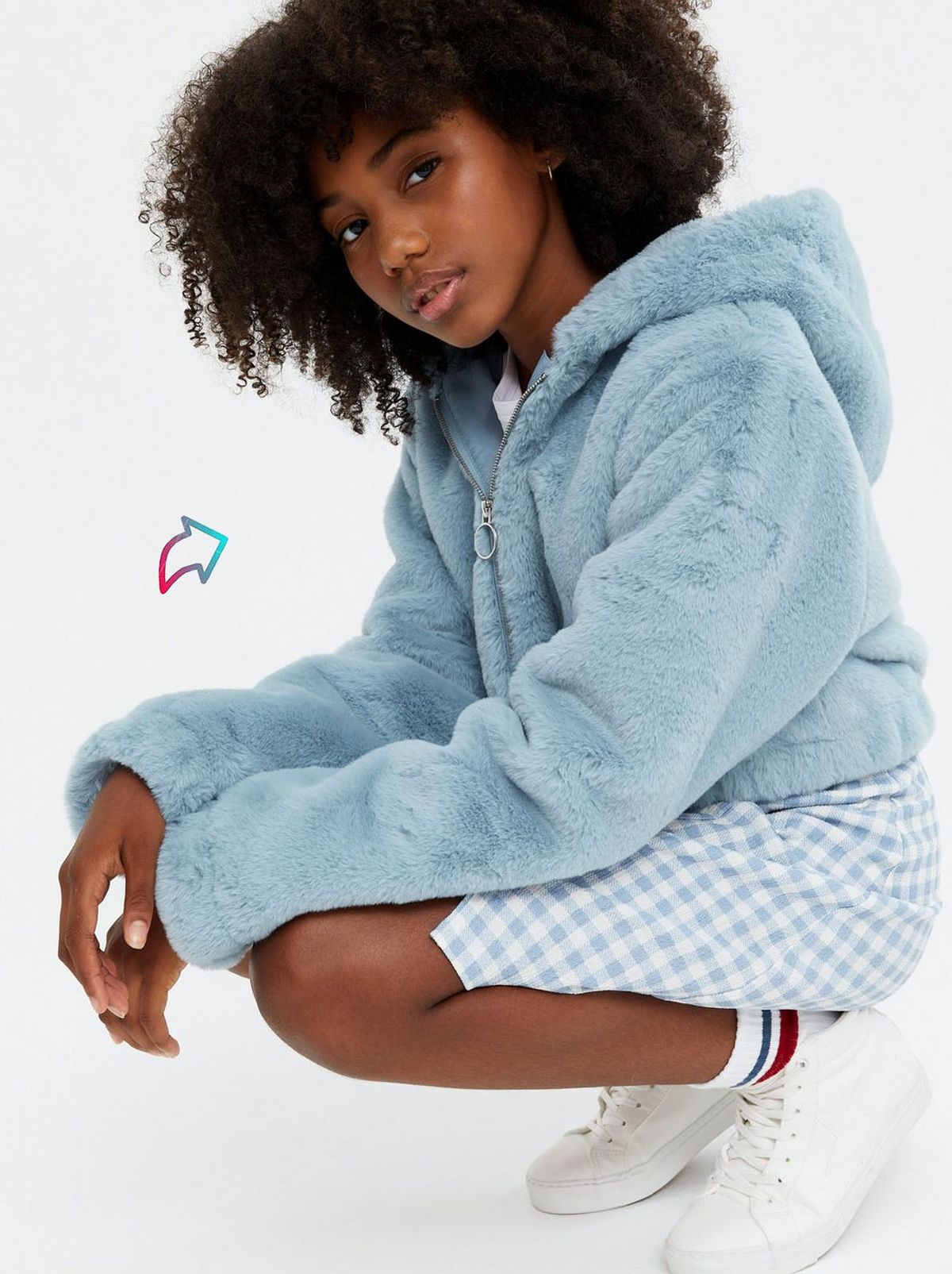 Girl wearing a pale blue faux fur hooded jacket, skirt and trainers	