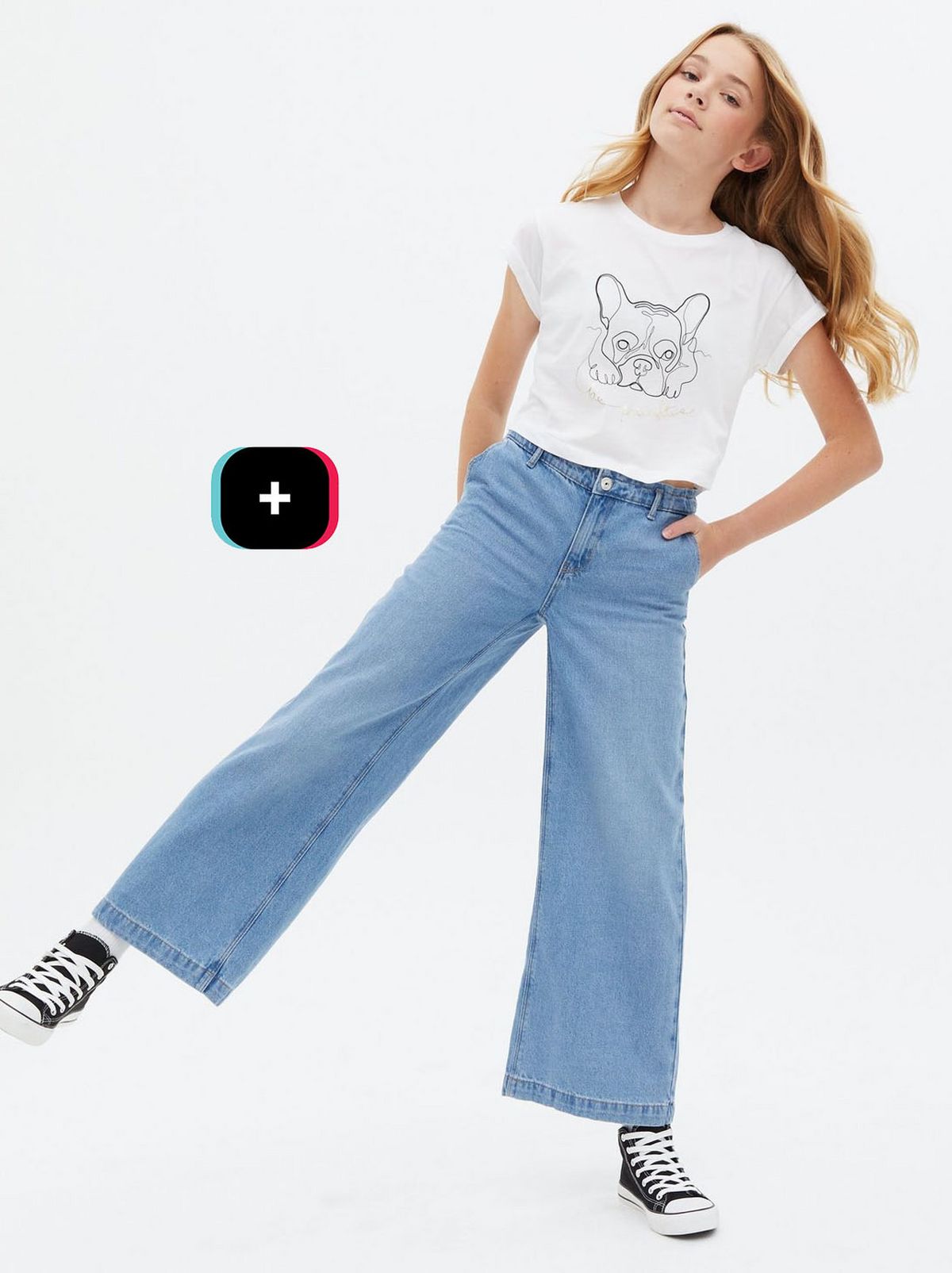 Girl wearing a white French bull dog logo t-shirt, jeans and trainers	