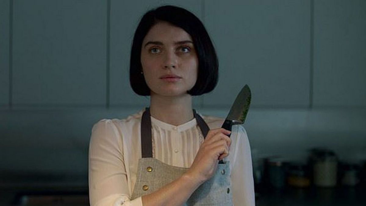 adele from movie behind her eyes stands in kitchen with knife