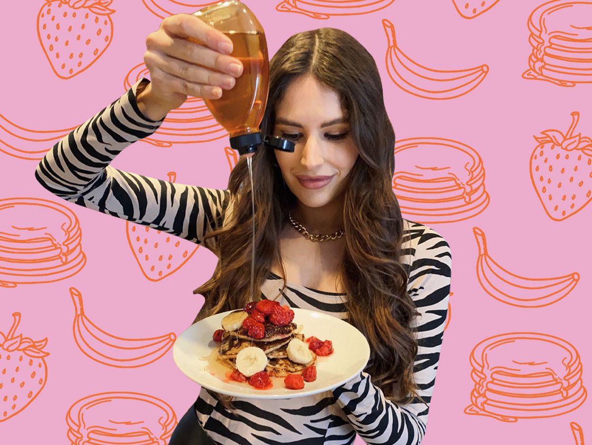 woman pours honey over plate of pancakes with raspberries and bananas