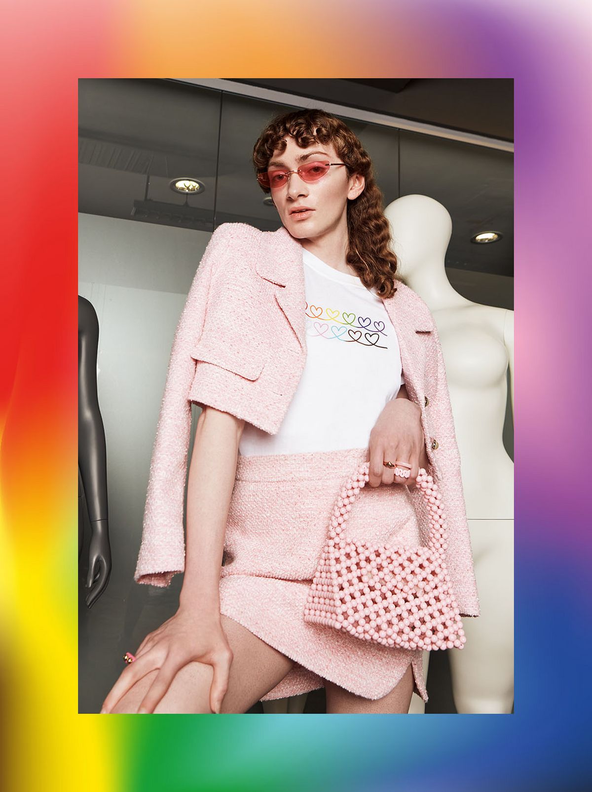Almanzo Ward is posing next to two mannequins wearing a matching pale pink blazer & mini skirt and holding a pink clutch	
