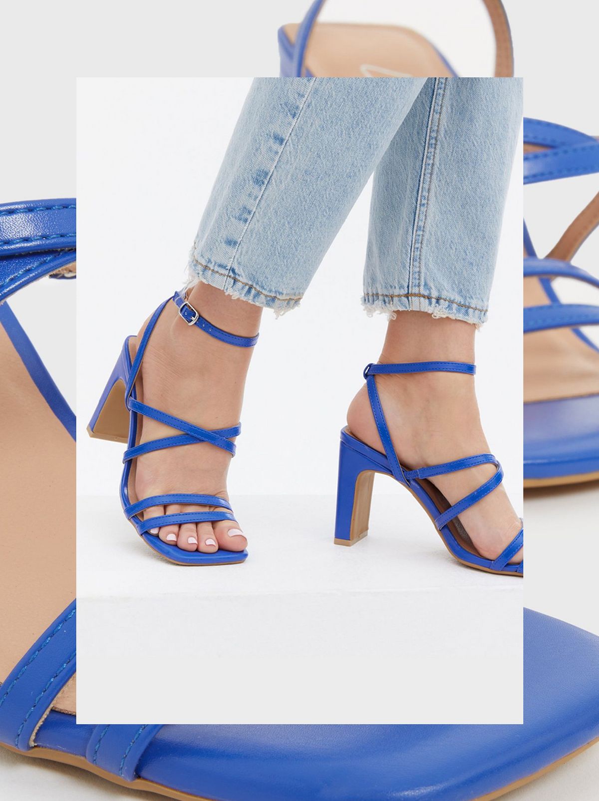 A person wears a pair of blue strappy block heel sandals and a pair of pale blue jeans