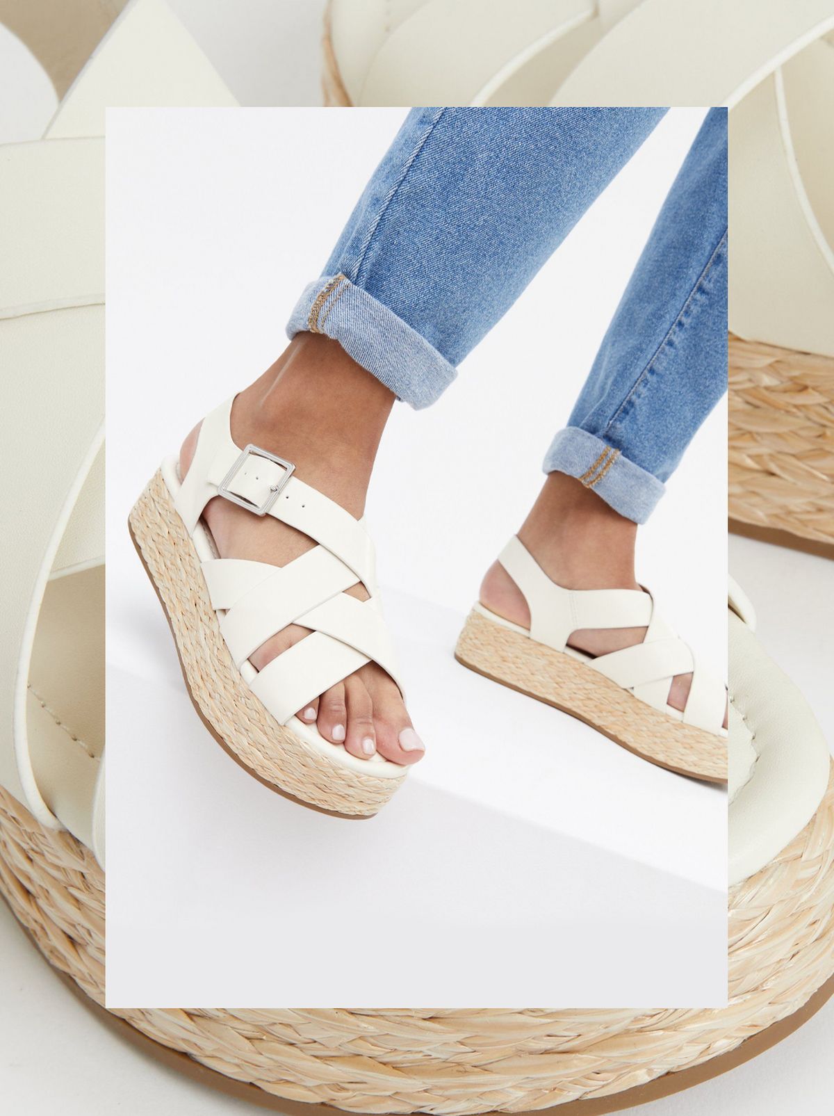 There is a person wearing a pair of off white strappy chunky sandals and a pair of blue jeans in front of a white background