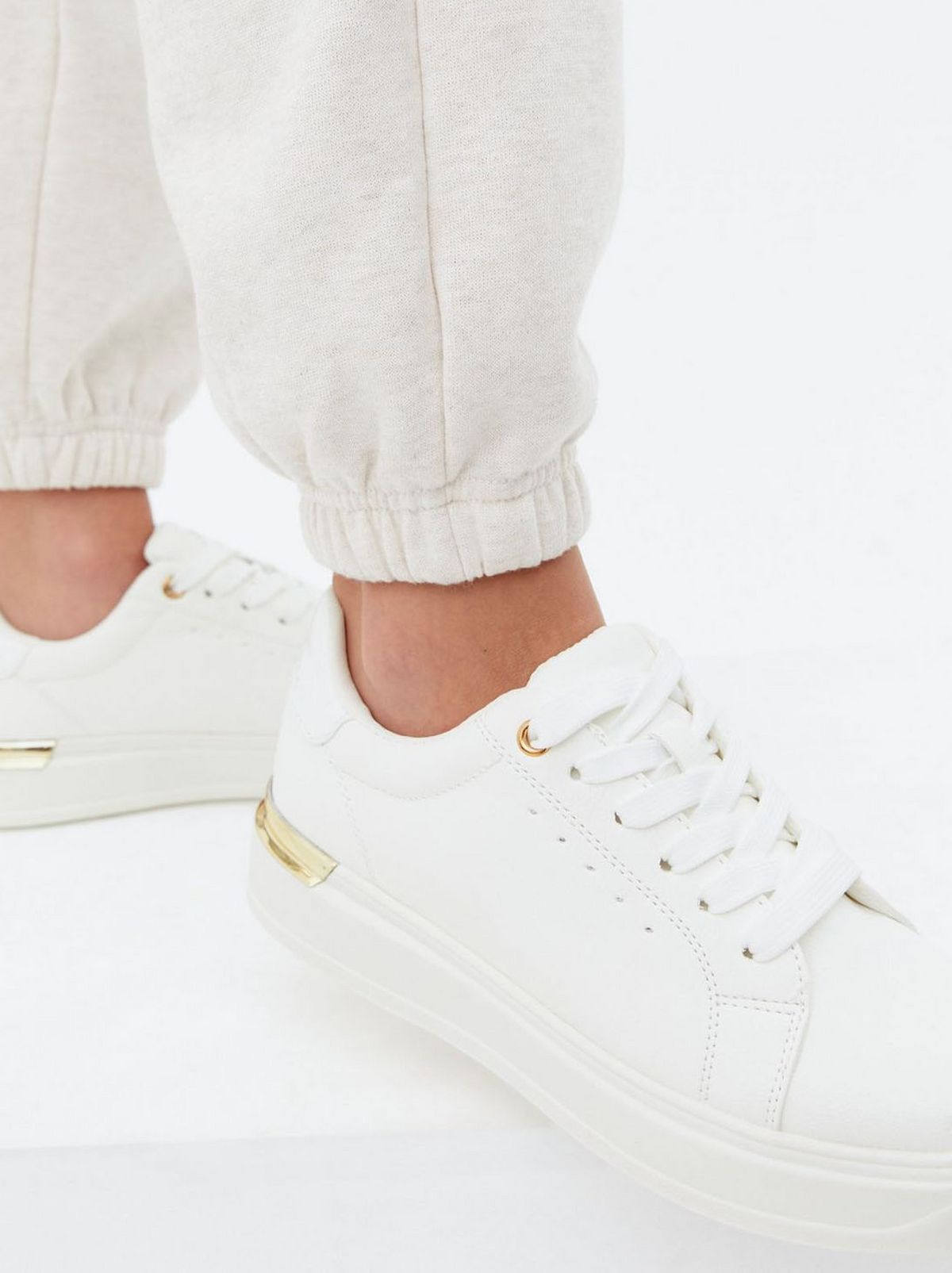 We see a person wearing a pair of grey joggers and a pair of chunky white trainers in front of a white background