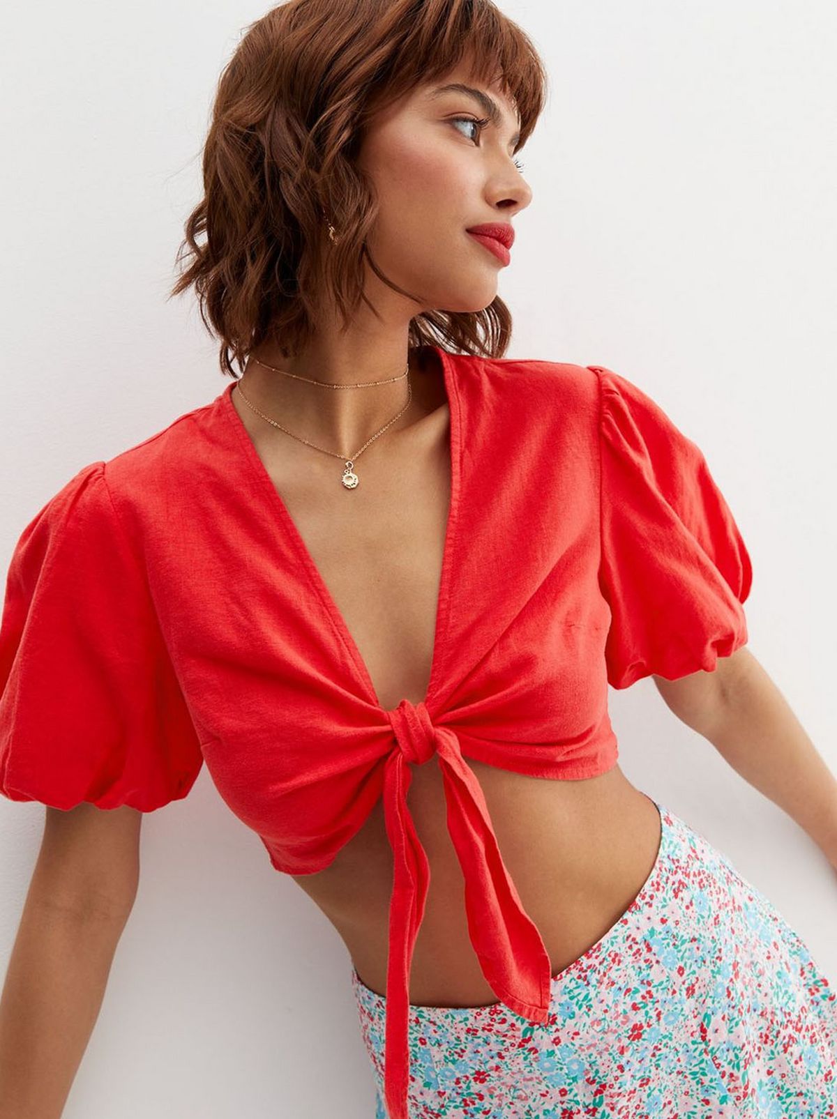A women stares into the distance wearing a patterned floral skirt and a bright red tie shirt with puff sleeves