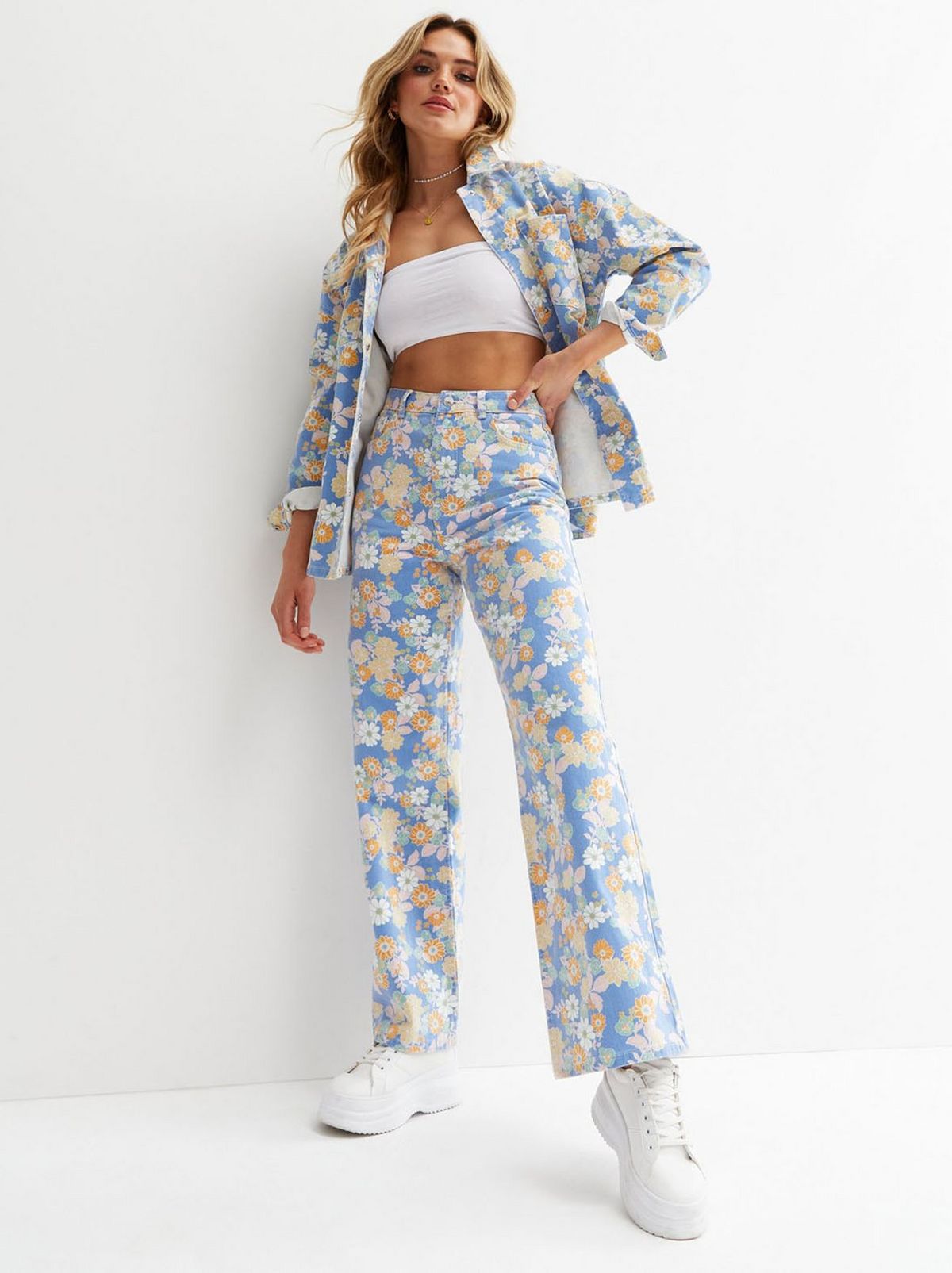 A women stands in front of a white background wearing a matching pair of floral wide leg jeans and a floral top 