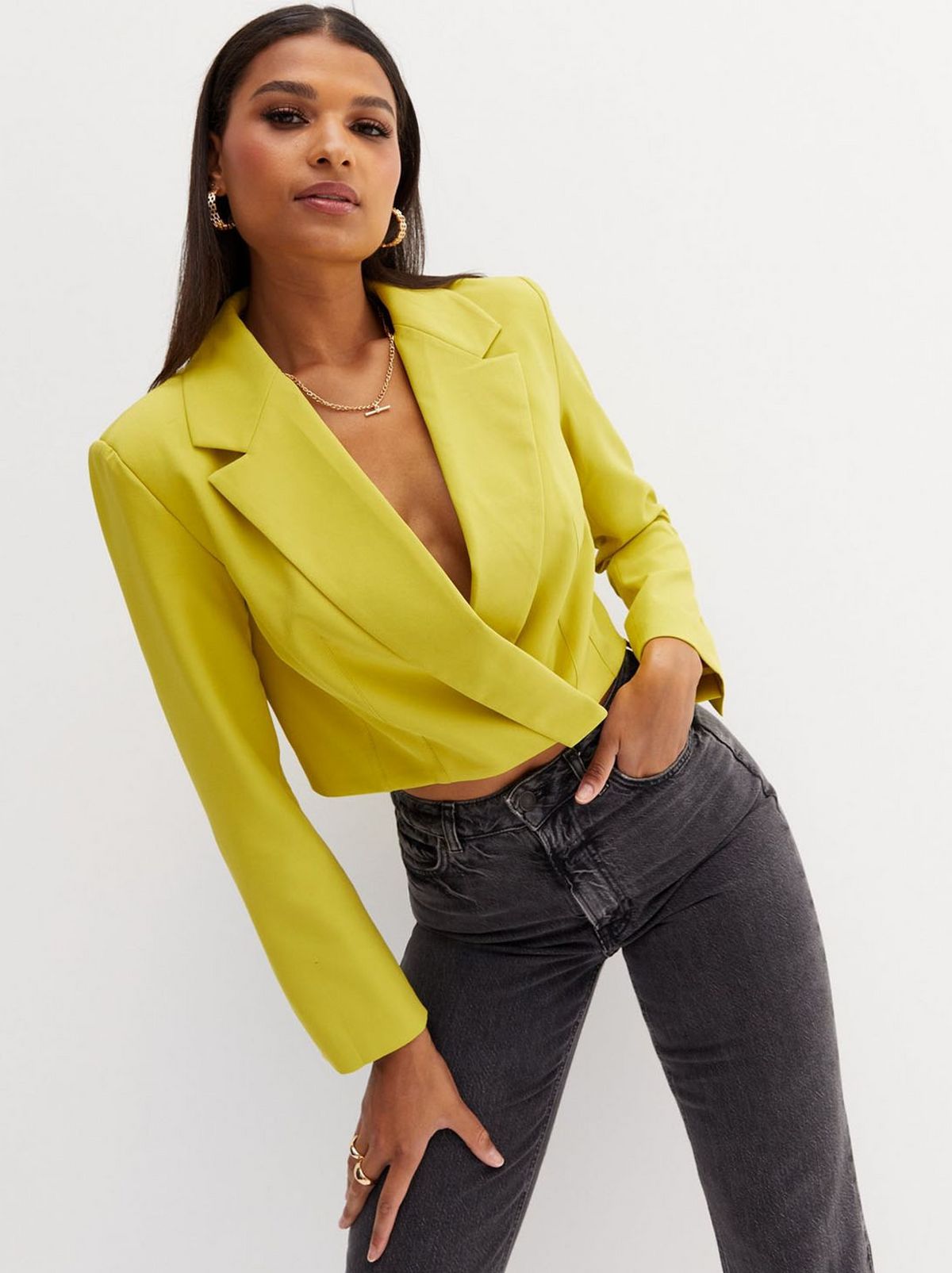 A women stands leaning to the side wearing a mustard blazer and a pair of black skinny jeans