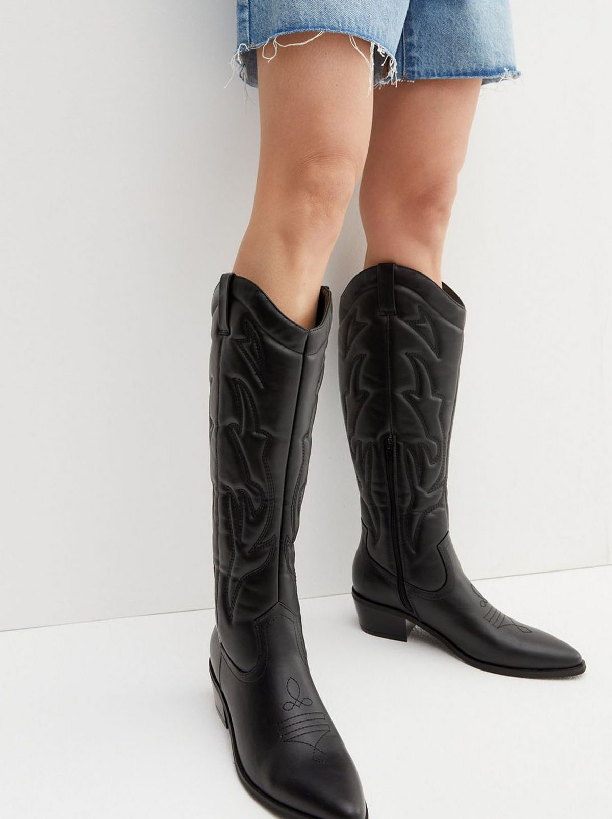 A black block heel cowboy boot is seen in front of a white background