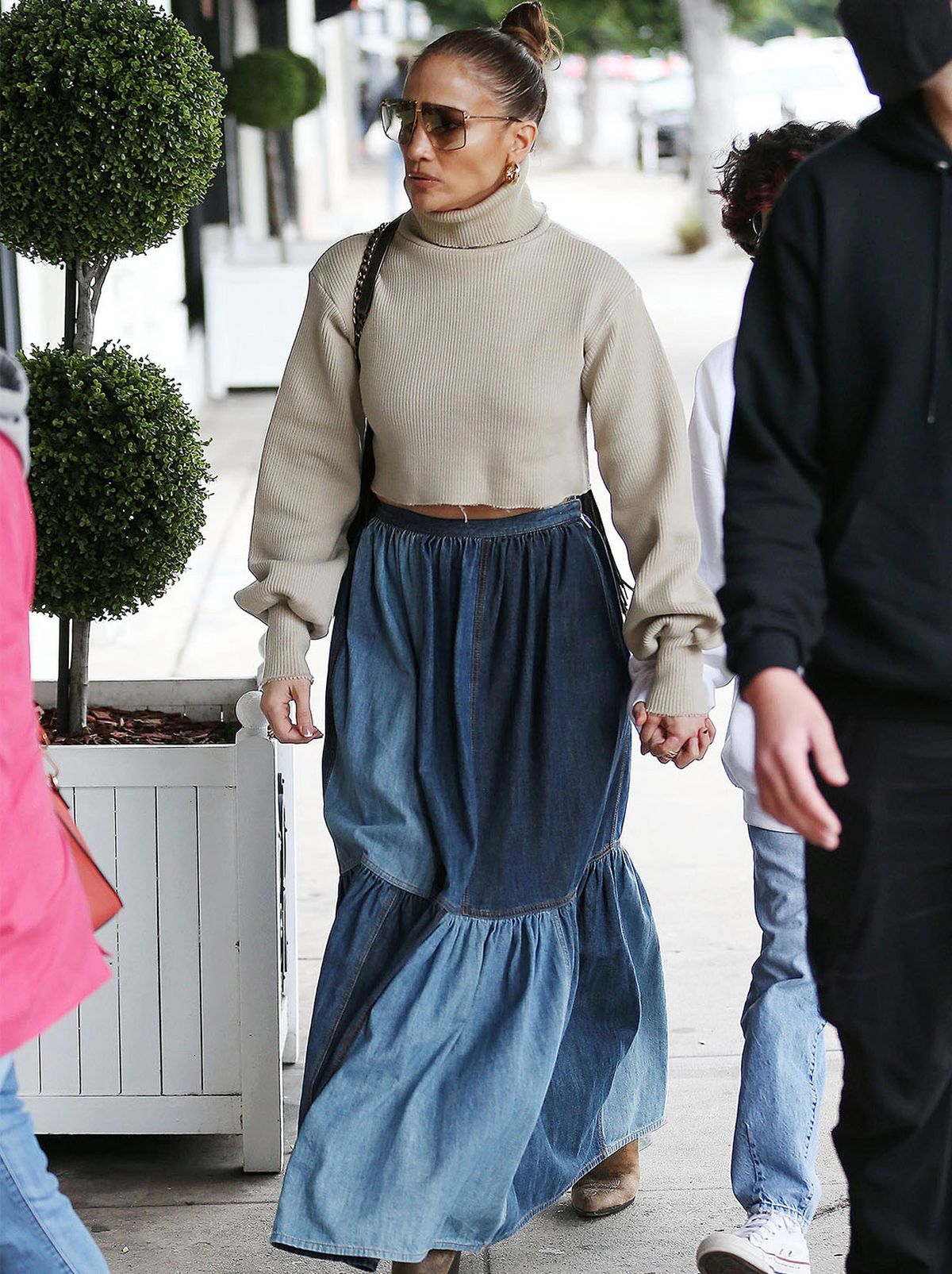 JLo walks down the street wearing a long denim skirt and a beige turtleneck jumper