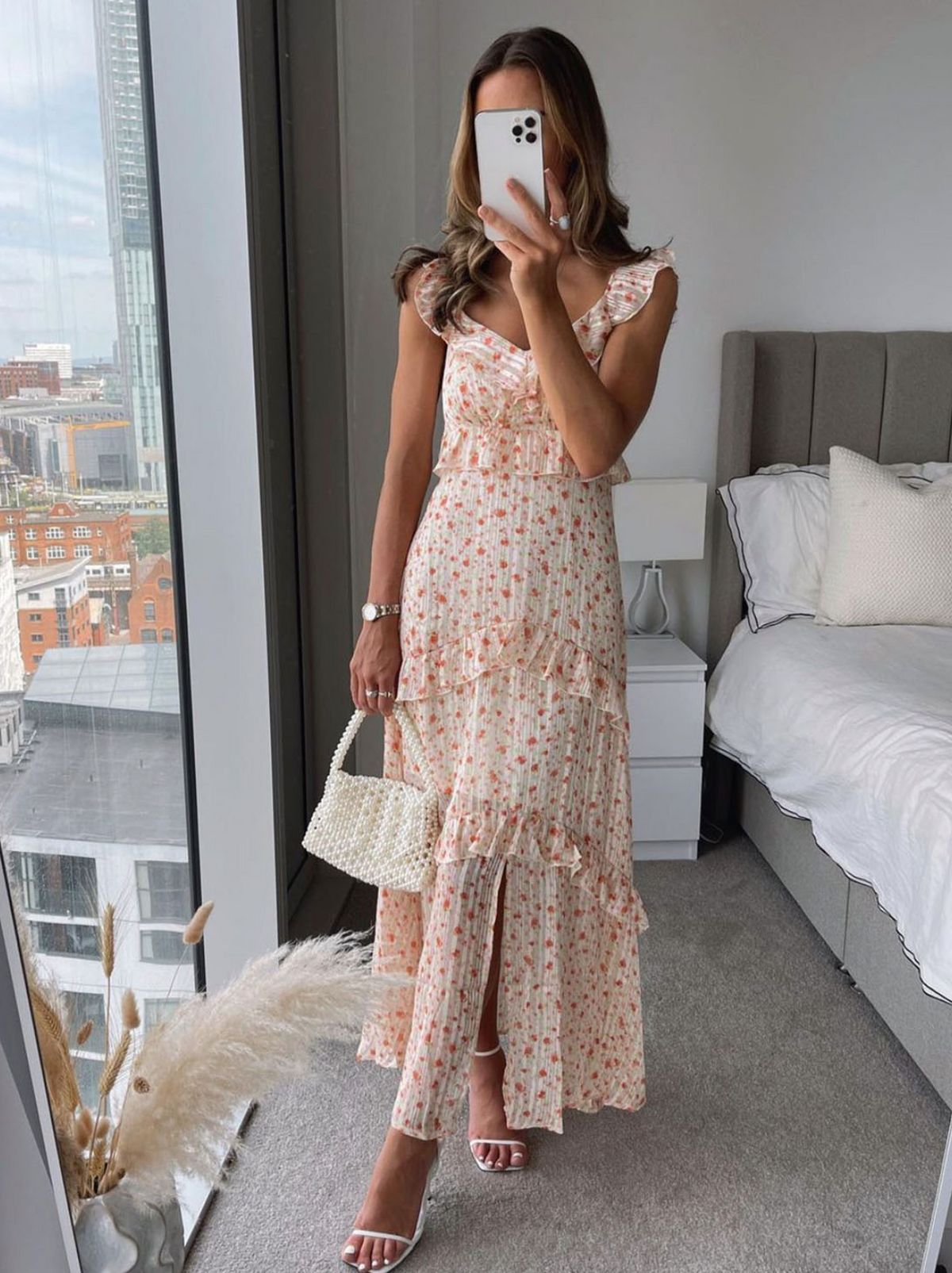 Emma Hothersall stands in a bedroom wearing a floral midi dress and holding a small handbag