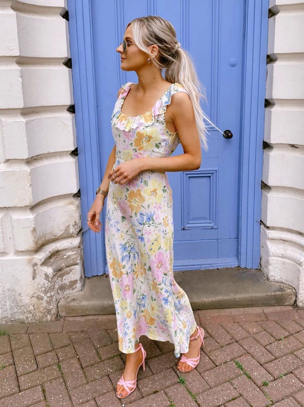 Joanne wears a floral white midi dress while standing in front of a blue door looking away from the camera