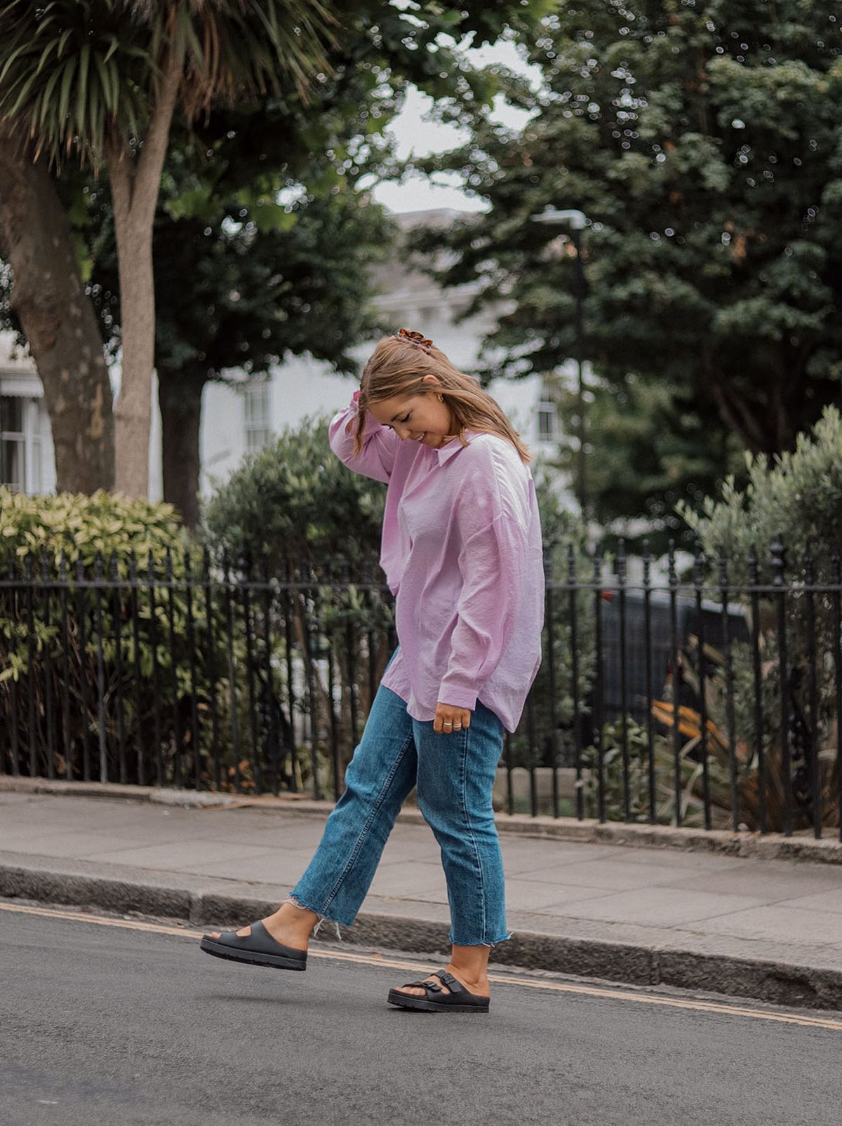 Poppy Deyes looks at the floor walking down the street while wearing an oversized lilac shirt and a pair of straight leg jeans