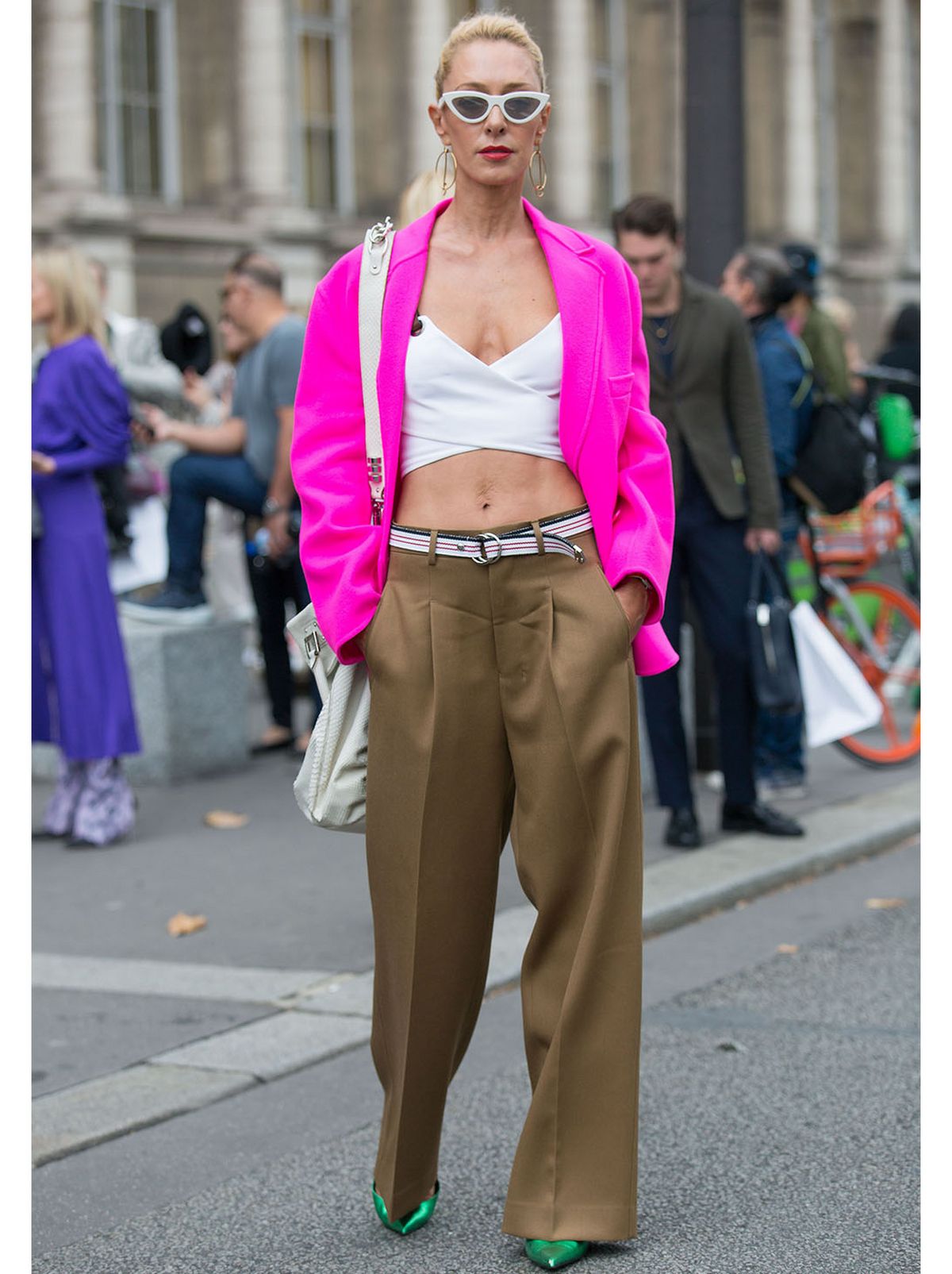 Woman walking wearing a pink blazer, crop top, brown wide leg trousers, green stilettos and sunglasses
