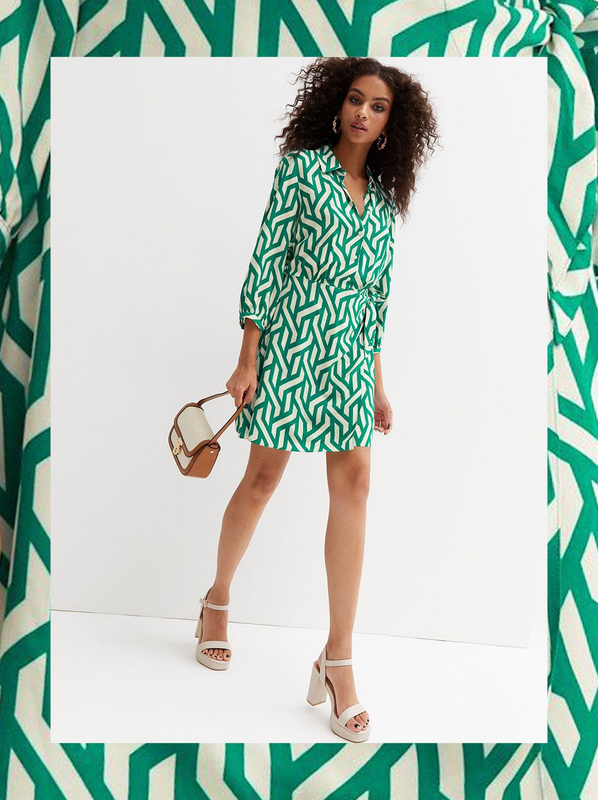 A women wears a green and white patterned long sleeve dress, looking at the camera and holding white clutch bag