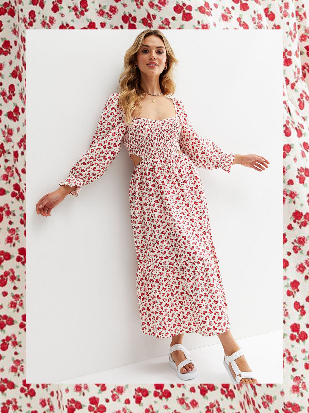 A women leans back on a white background wearing a long sleeve white and red maxi dress, holding her arms out looking at the camera