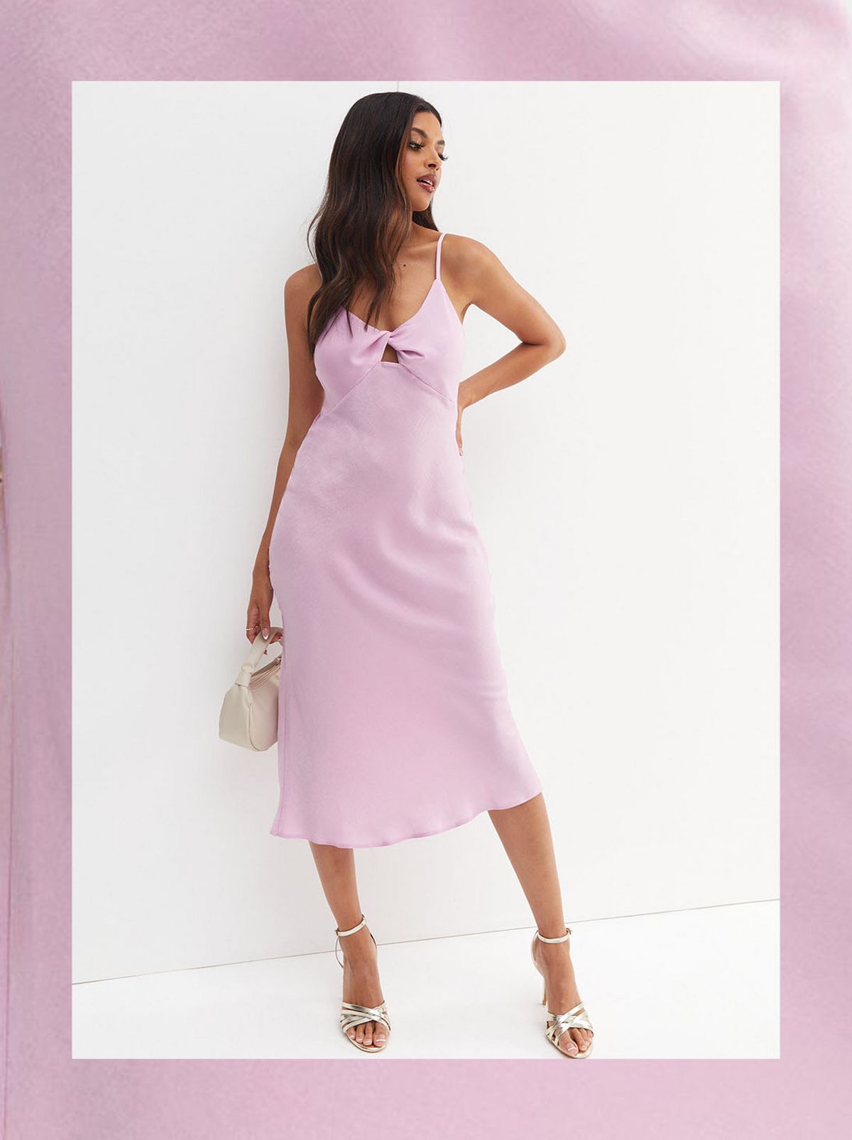 A women stands with her hand on her hip, looking over her shoulder while wearing a strappy lilac dress