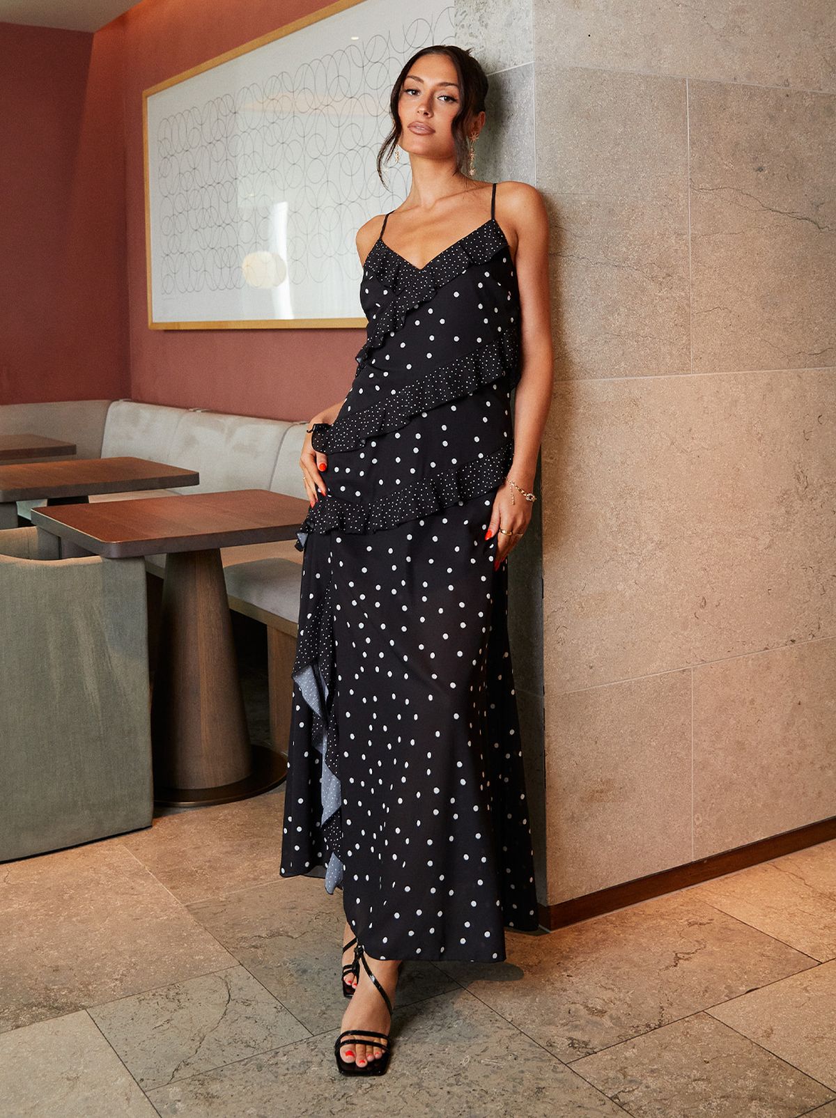Liana Tambini leaning against a wall, wearing a black and white spotted dress and heels	