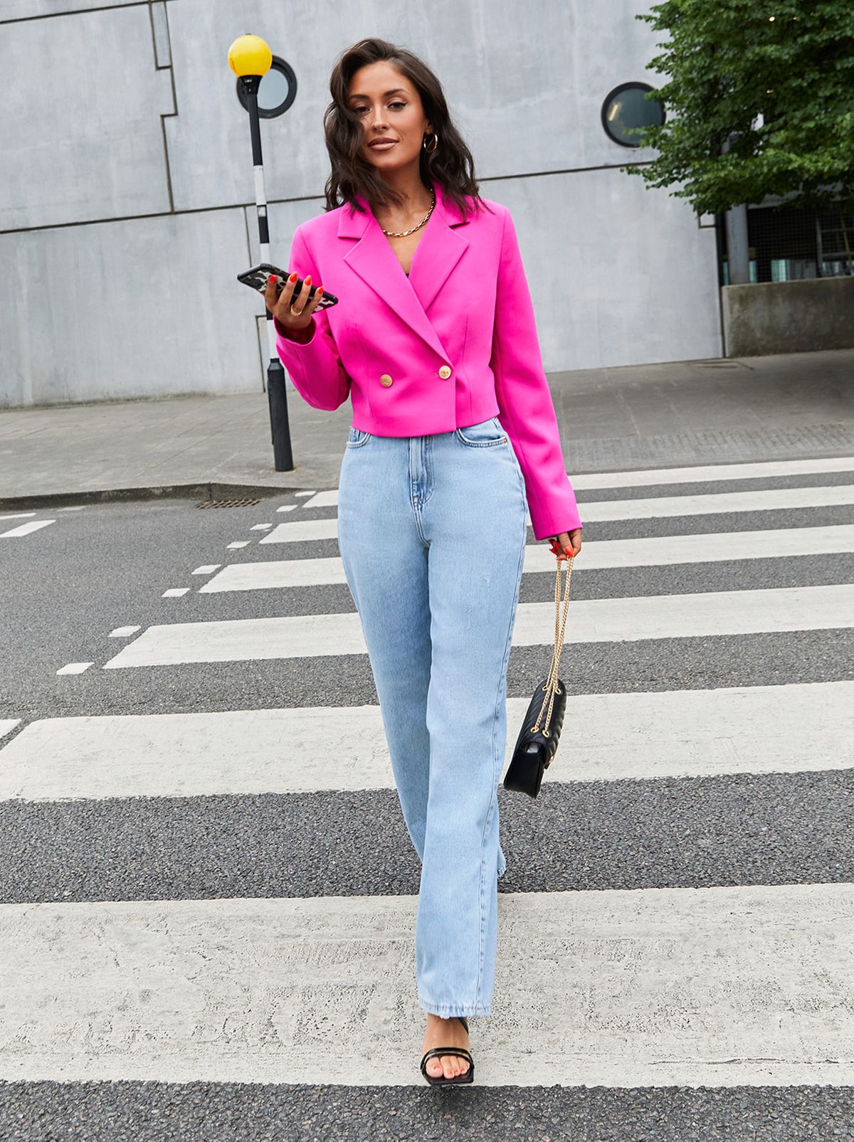 Liana Tambini on a zebra crossing wearing a pink blazer, blue jeans, heels and holding a handbag	