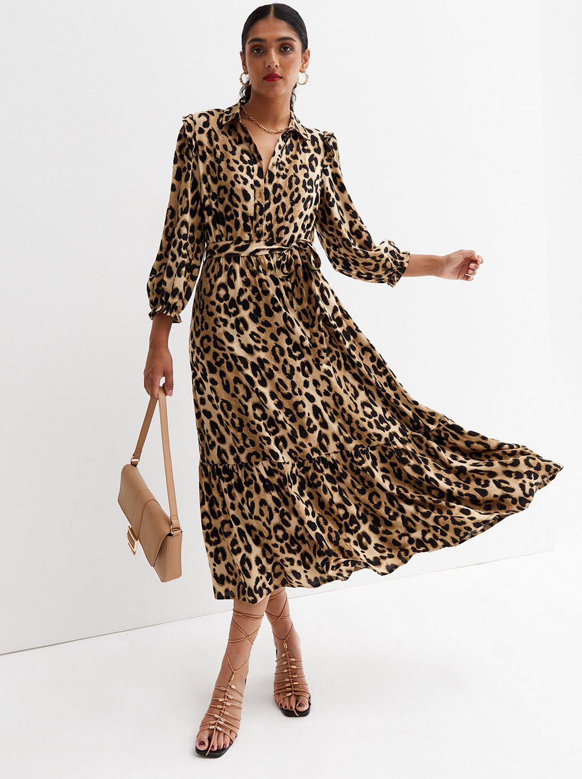 A model walks towards the camera wearing a brown leopard print midi dress and holding a tan handbag