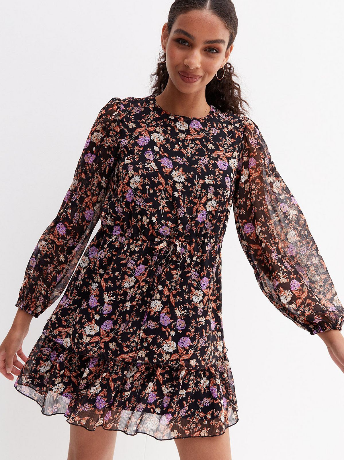 A model stands in front of a white background smiling at the camera wearing a black floral puff sleeve midi dress 