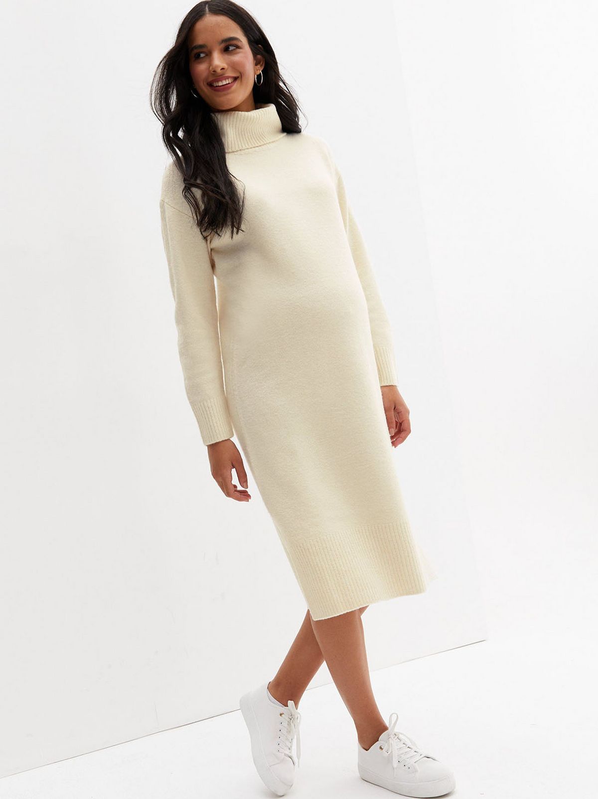A model walks away from the camera in front of a white background while wearing a maternity cream knit roll neck midi dress