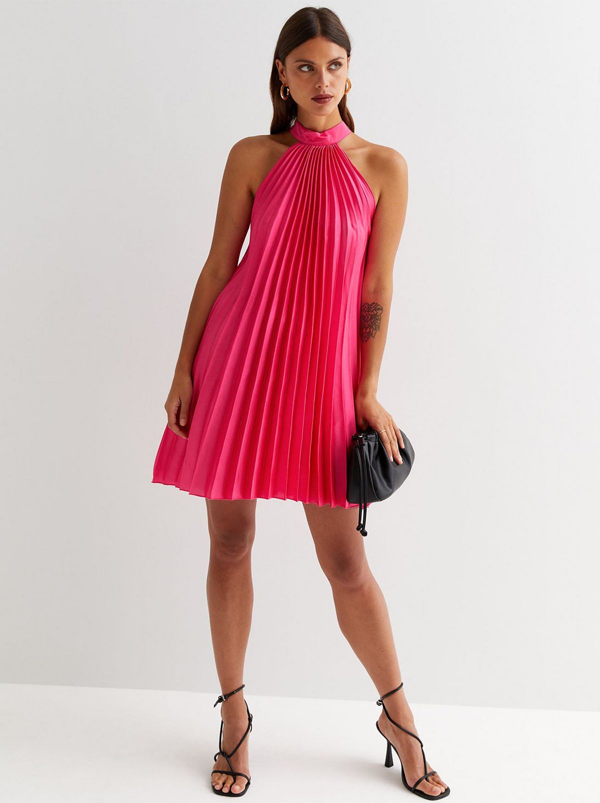 A model stands facing the camera while looking down while wearing a bright pink halter dress