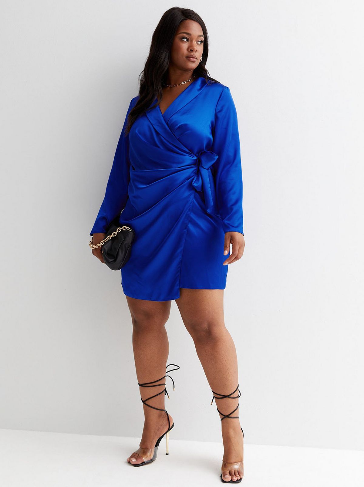 A model stands looking away from the camera, wearing a blue wrap dress and a pair of strappy heels
