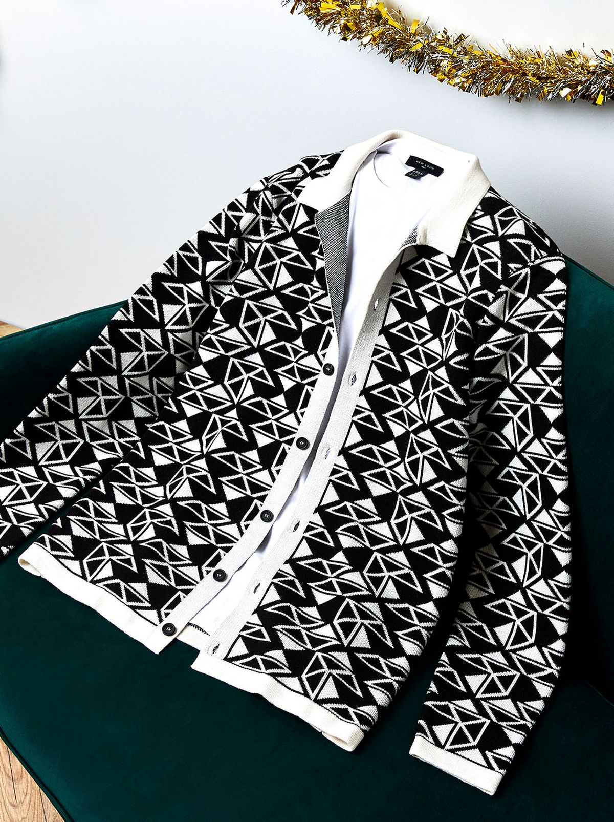 There is a patterned black blazer with a collared shirt lying on a green sofa, with a corner of tinsel hanging in the top right