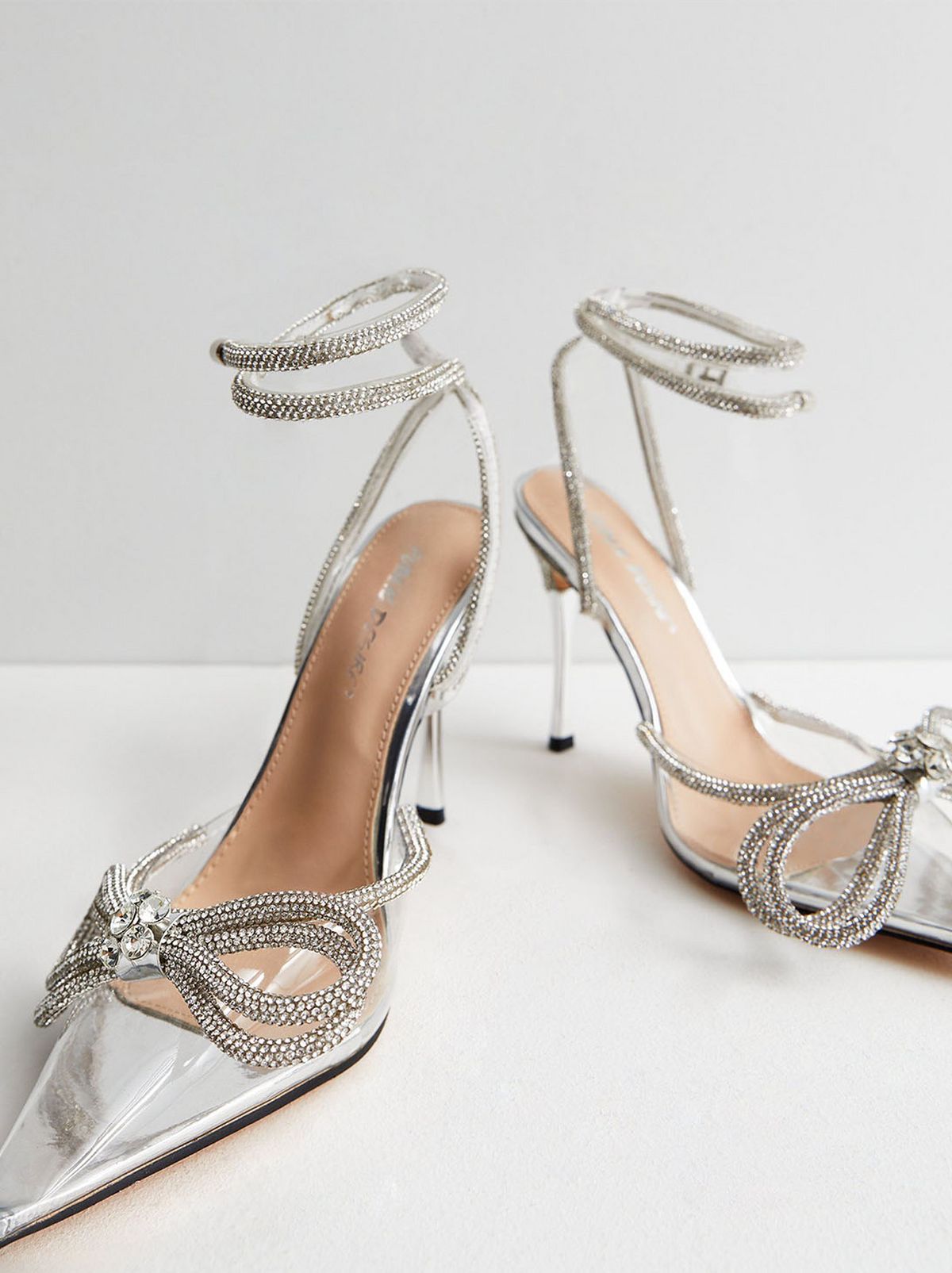 A pair of silver diamante stiletto heeled sandals are standing in the edge of a white room