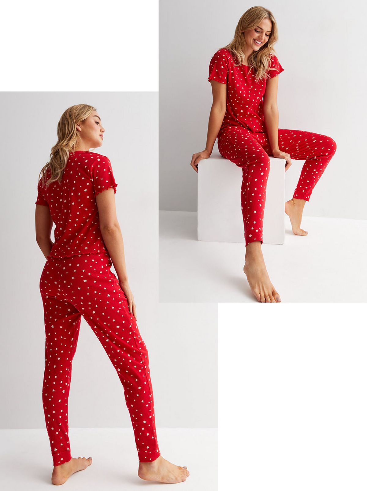 A model sits on a white block in front of a white background, looking at the floor and smiling as she wears a red star print matching pyjama set