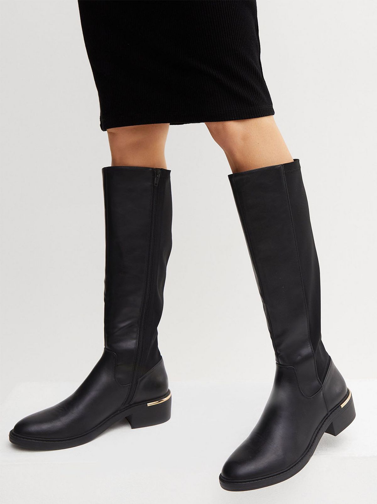 A person is wearing a pair of black knee high boots in front of a white background