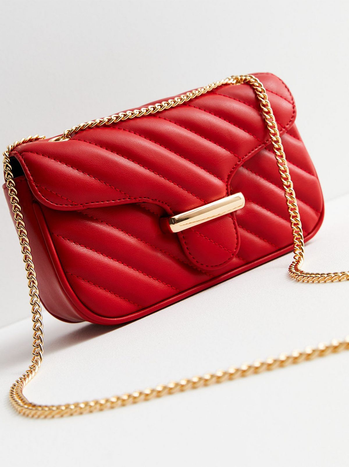 A red leather look quilted chain strap shoulder bag is sitting on a white floor in front of a white background