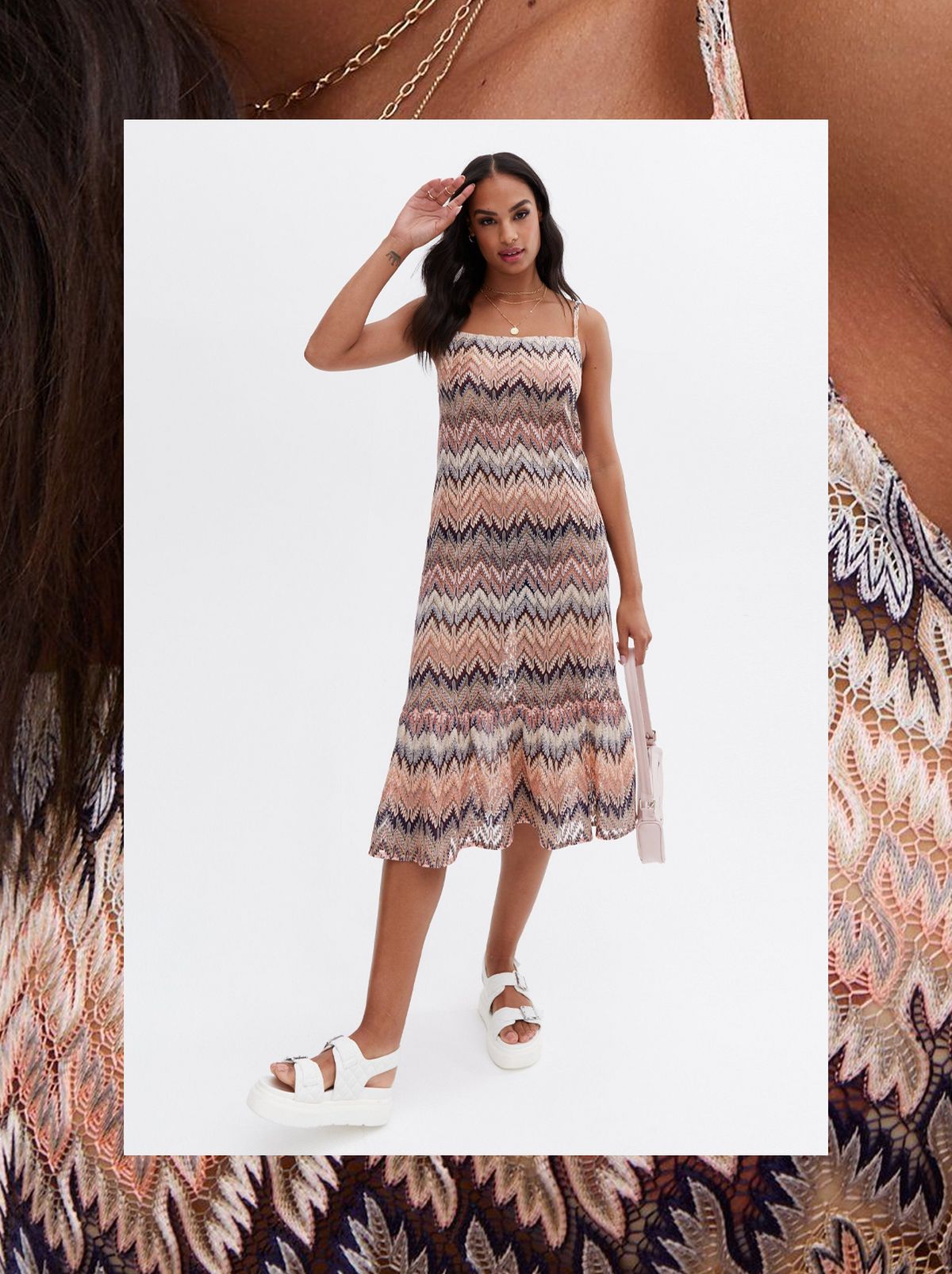 A women stands in front of a white background brushing her hair out of her face while wearing a patterned strappy midi dress