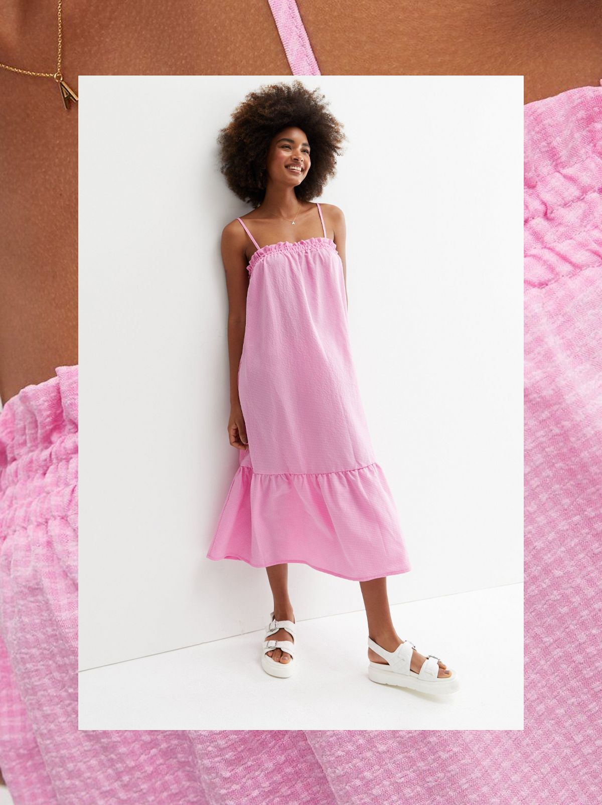 A women leans on a wall looking away from the camera wearing a pink tiered midi dress