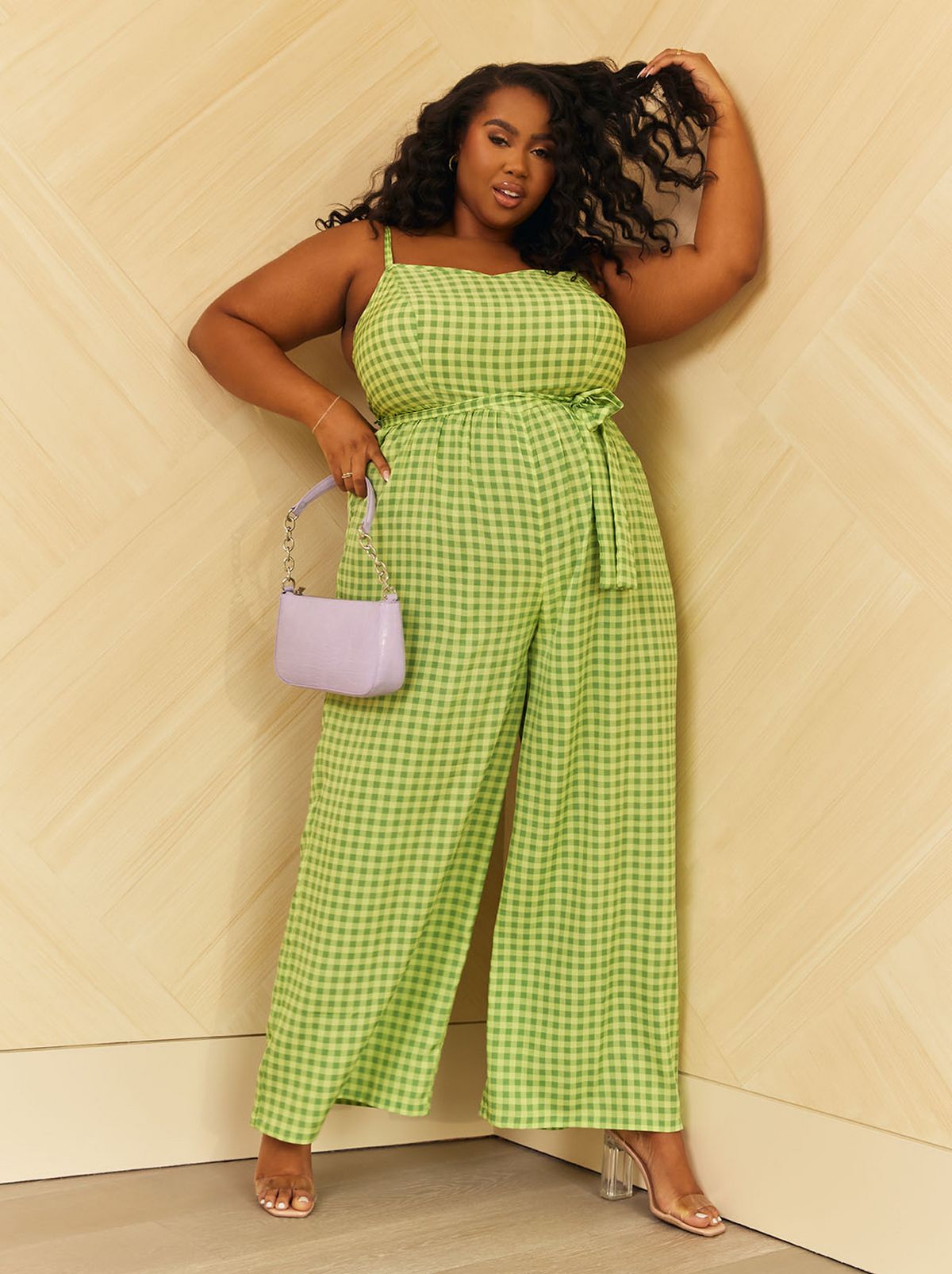 Lauren Nicole is leaning in the corner of the room wearing a lime green playsuit and holding a silver handbag